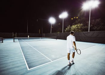 Tennis teammates practicing together on outdoor court at night