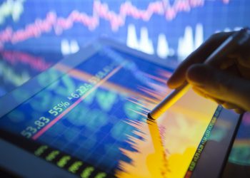 A hand using a digital tablet showing stock fluctuations