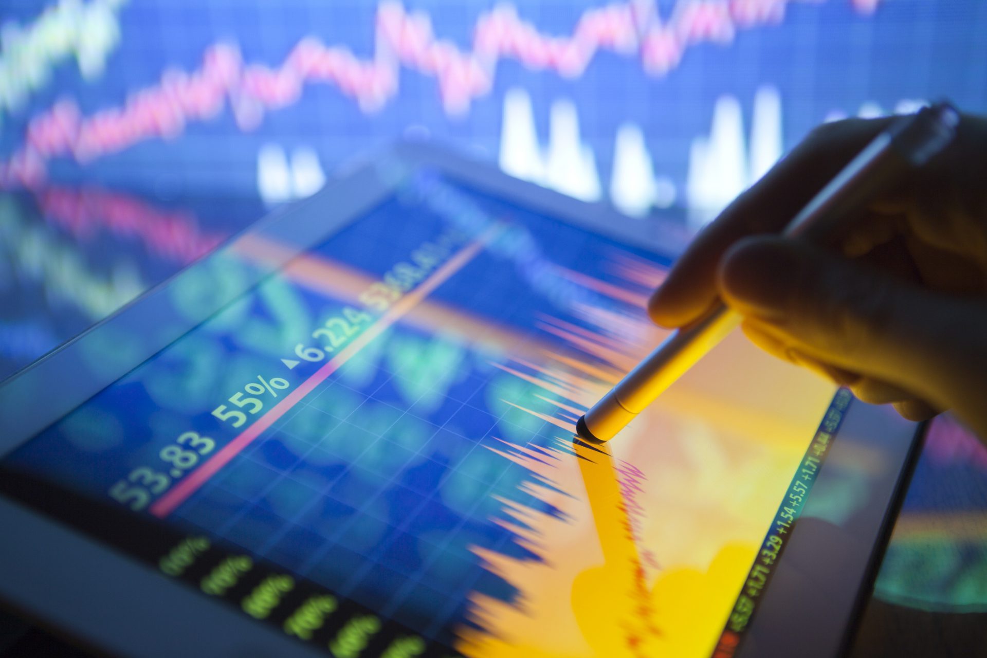 A hand using a digital tablet showing stock fluctuations
