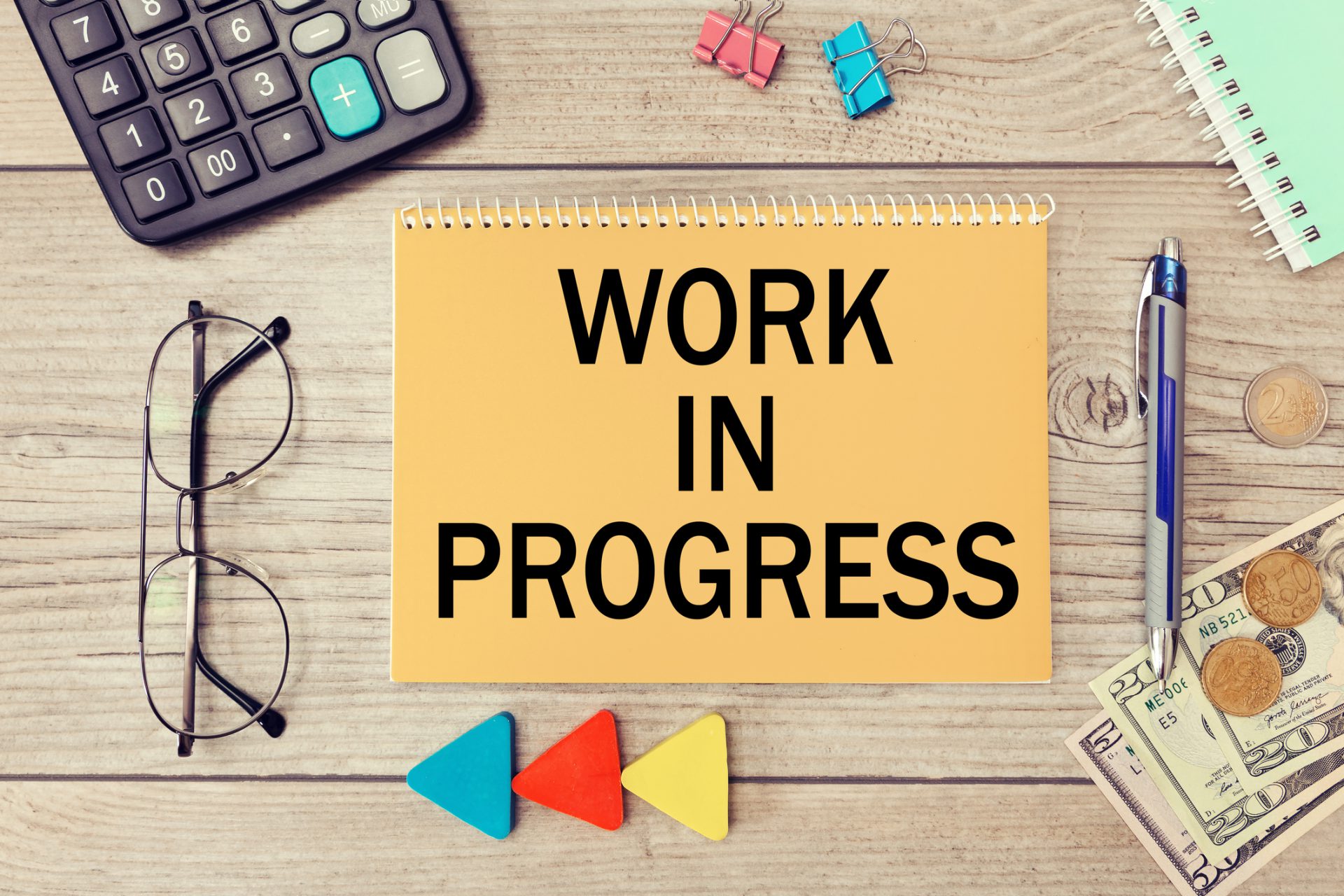 Blank notepad with text Work in progress on wooden surface, calculator, glasses, money