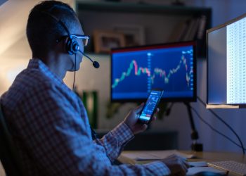 Man looking at currency trading app on his smart phone from his home office