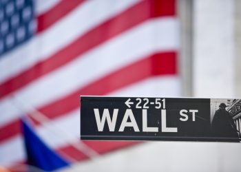 Sign on Wall Street and American flag.