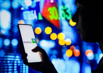 BRAZIL - 2022/04/04: In this photo illustration, a woman's silhouette holds a smartphone with the Saudi Arabian Oil Company (Aramco) logo displayed on the screen. (Photo Illustration by Rafael Henrique/SOPA Images/LightRocket via Getty Images)