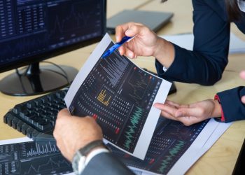 Brokers discussing trading strategy, holding papers with financial data, pointing pen at charts. Cropped shot. Broker job or stock market exchange concept