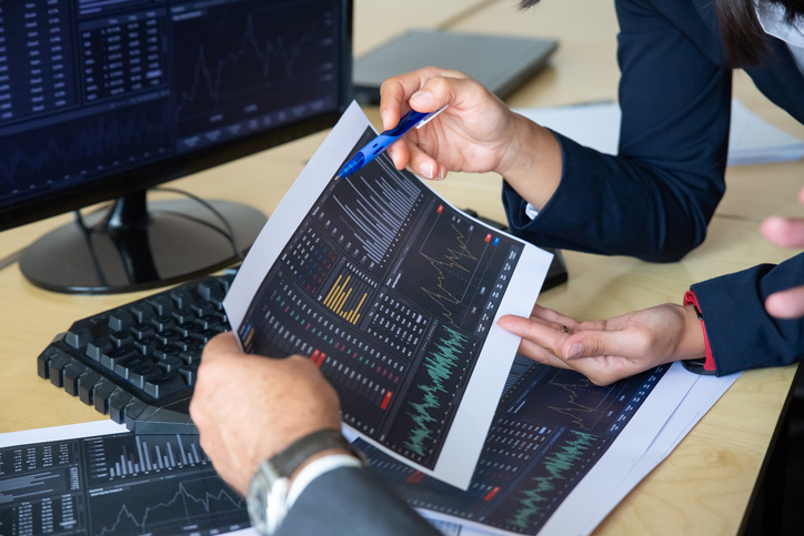 Brokers discussing trading strategy, holding papers with financial data, pointing pen at charts. Cropped shot. Broker job or stock market exchange concept
