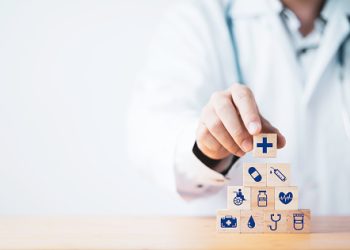Doctor putting and stacking wooden block cube which print screen health care and medical icons for healthy and wellness concept.
