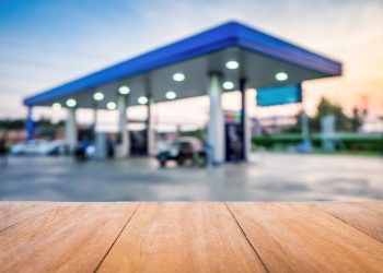 Wood table in front view of the petrol station at sunset blur background. Brown wooden desk in front view of the gas station. Empty counter beside fuel pump transportation service.