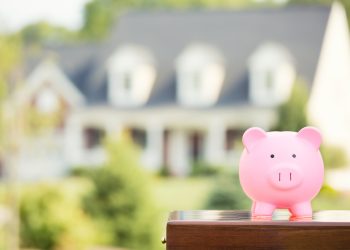 Real estate sale, home savings, loans market concept. Housing industry mortgage plan and residential tax saving strategy. Piggy bank isolated outside home on background. Focus on piggybank. Homeowner