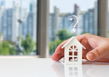 Real estate questions answers concept. Hand shows a house with a question mark on a blurred background.