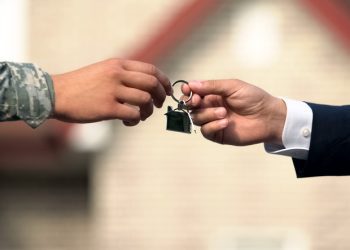 Man in business suit giving house key to man in military uniform, state support