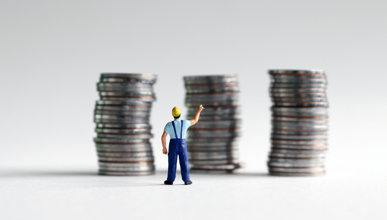 A miniature man reaching for a pile of three coins.